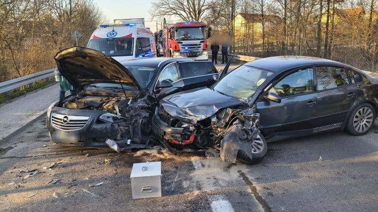 Zderzenie dw&oacute;ch samochod&oacute;w na drodze krajowej, uszkodzone pojazdy i służby ratunkowe na miejscu.