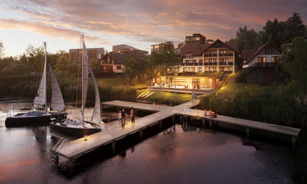 Widok na jezioro z pomostem i łodziami, w tle nowoczesne apartamenty nad wodą o zachodzie słońca.