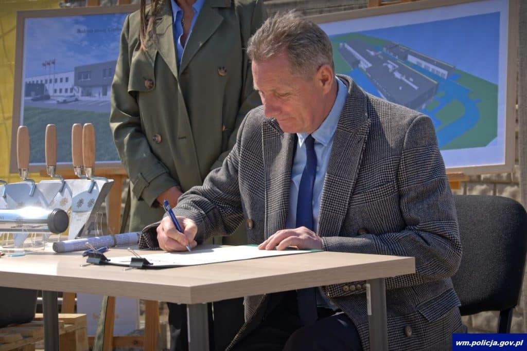 Mężczyzna podpisuje dokumenty podczas uroczystości rozpoczęcia budowy nowej komendy policji w Ostr&oacute;dzie.