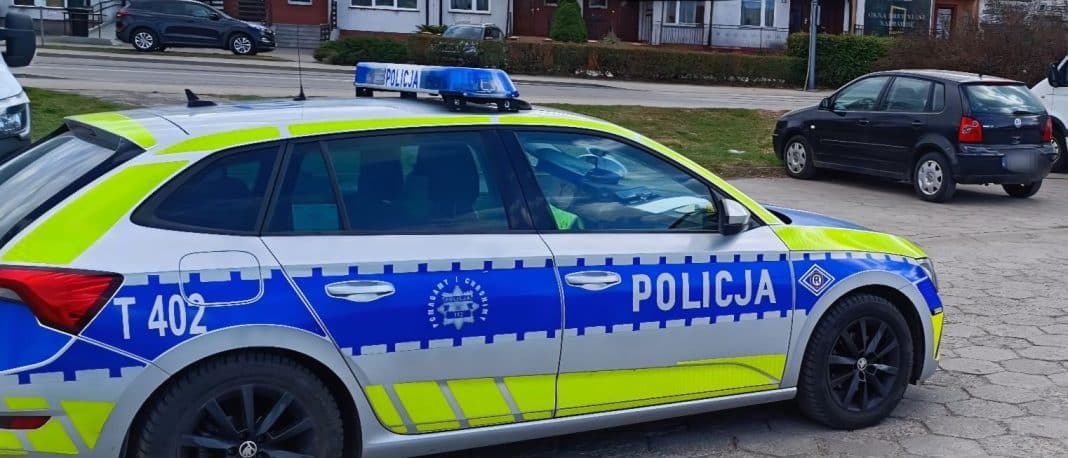 Policja na ulicy, radiow&oacute;z w centrum miasta, w tle budynki mieszkalne.