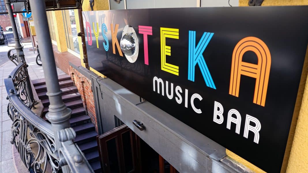 Widok na wejście do nowego klubu Dyskoteka Music Bar na olsztyńskiej starówce, z kolorowym napisem na szyldzie.