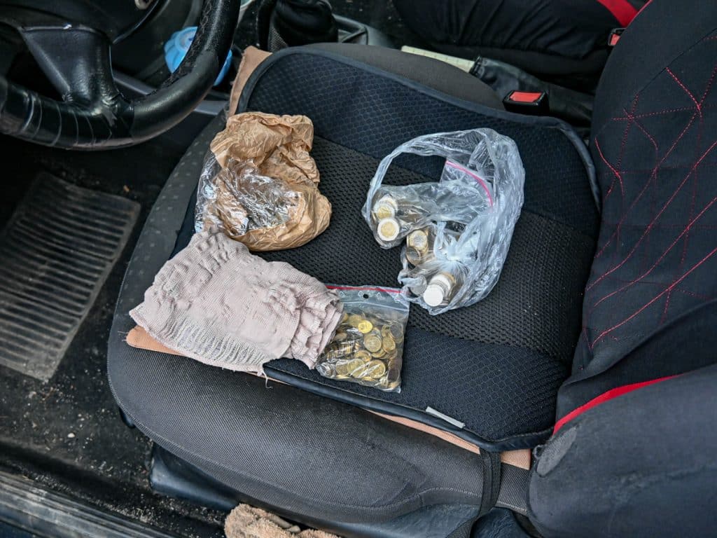 Na zdjęciu widoczny samoch&oacute;d z zawartością na siedzeniu, w tym plastikowe worki z monetami i papierowe torby.