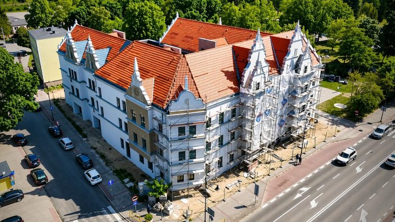 Widok na niedokończony budynek Domu Kultury w Piszu, otoczony drzewami i ulicami miasta.