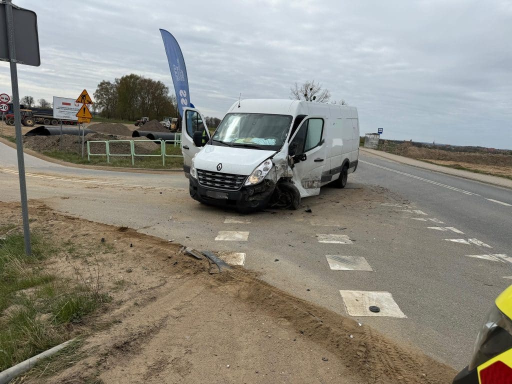 Uszkodzony samoch&oacute;d dostawczy na drodze, wypadł z jezdni i leży na poboczu, w tle budowa i pojazdy robocze.
