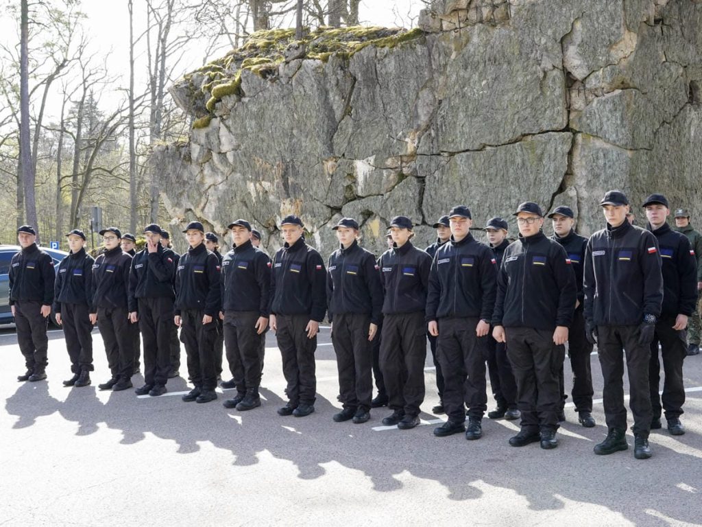 Grupa młodych ludzi w uniformach stojąca na tle skały podczas wydarzenia na Mazurach.