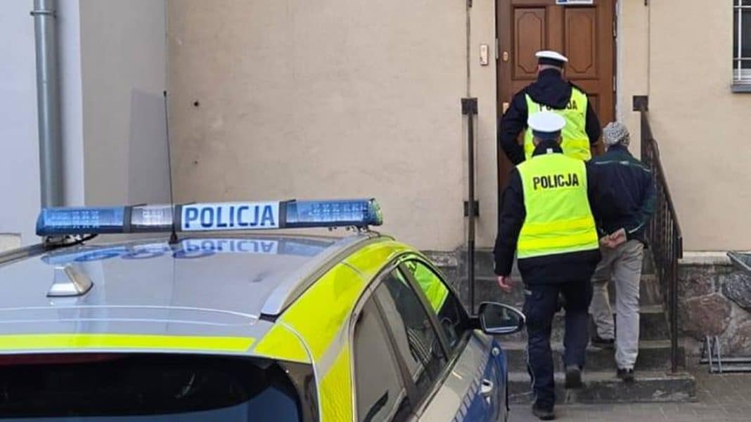 Policjanci prowadzący kontrolę drogową przy wejściu do budynku, na pierwszym planie radiow&oacute;z policyjny.