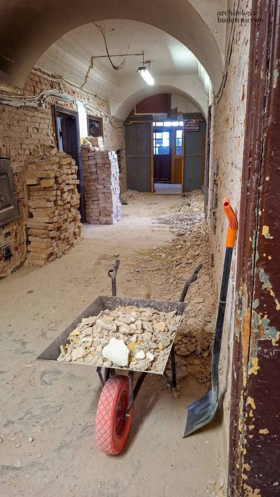 Wnętrze zabytkowego koszarowca w trakcie remontu, widoczne ceglane mury i prace budowlane.