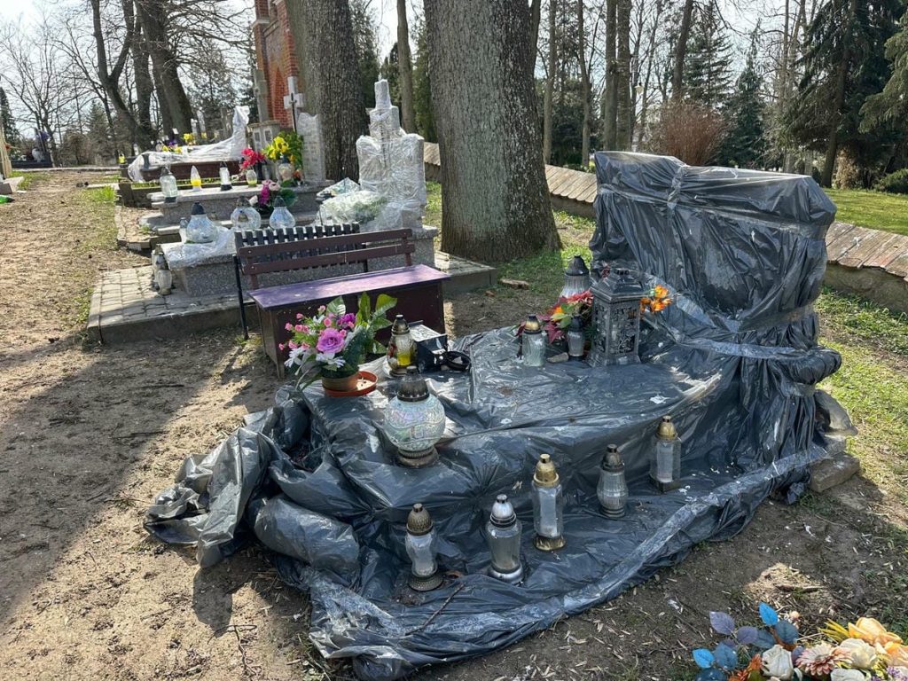Nagrobek owinięty folią, wok&oacute;ł lampiony i kwiaty na cmentarzu w Jezioranach.