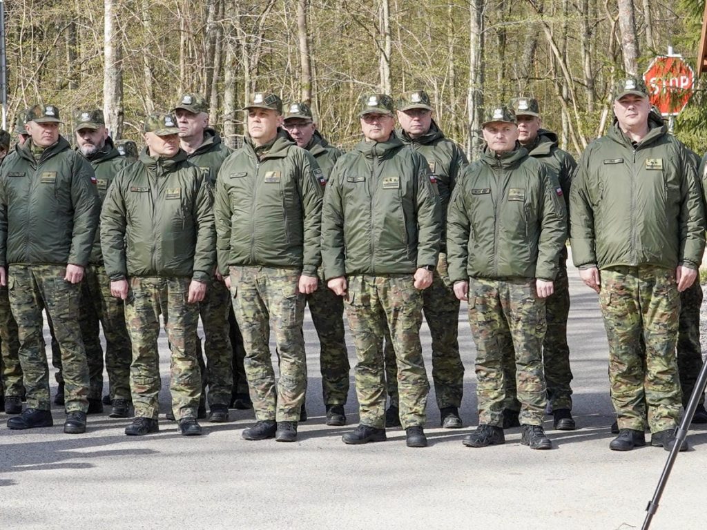 Grupa funkcjonariuszy w mundurach stojąca na zewnątrz, w tle las i znaki drogowe.
