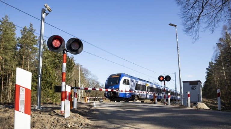 Przejazd kolejowy z zamkniętymi rogatkami i pociąg na tle lasu, w regionie warmińsko-mazurskim.