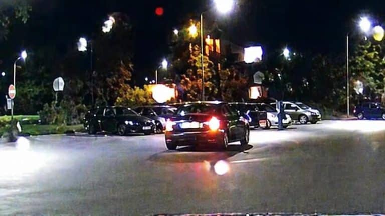 Zdjęcie policyjnego patrolu na ulicy w nocy, w tle kilka zaparkowanych samochod&oacute;w, widoczny patrol policyjny.