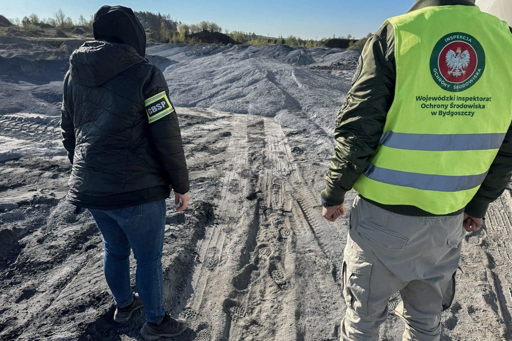 Funkcjonariusze CBŚP na miejscu akcji w terenie, w tle ślady po pojazdach i ziemia.