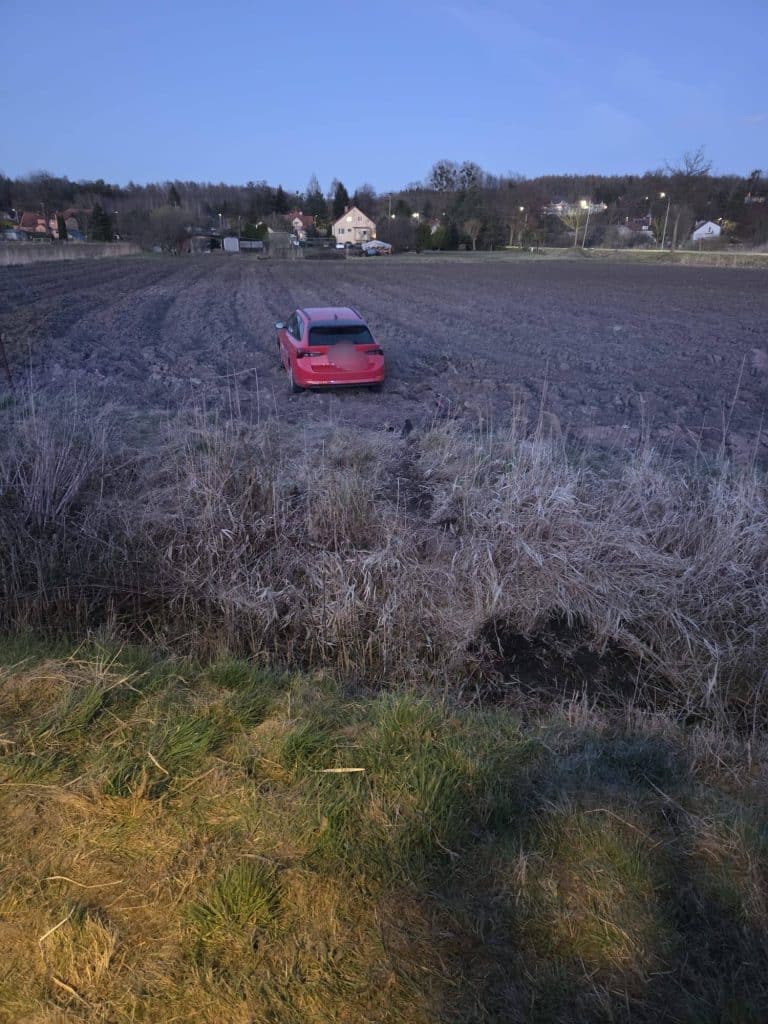 Samoch&oacute;d osobowy na polu po wypadku, widok z daleka na pole i okoliczne domy.