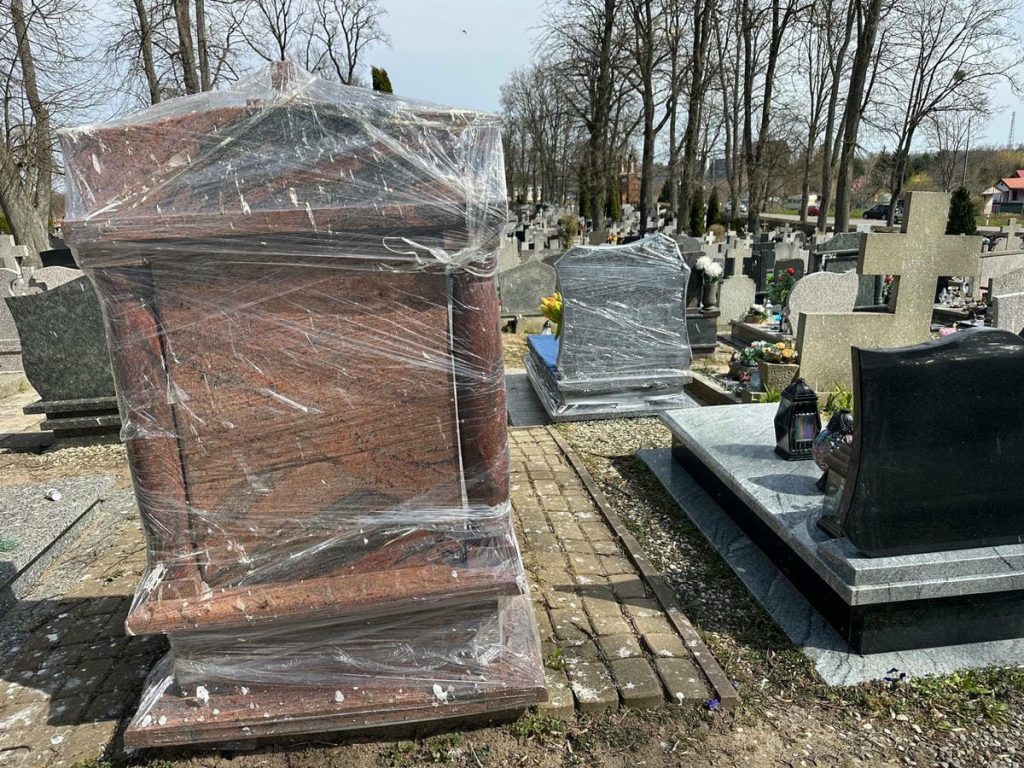 Na cmentarzu w Jezioranach owinięte folią nagrobki, wok&oacute;ł liczne ptaki i zanieczyszczenia.