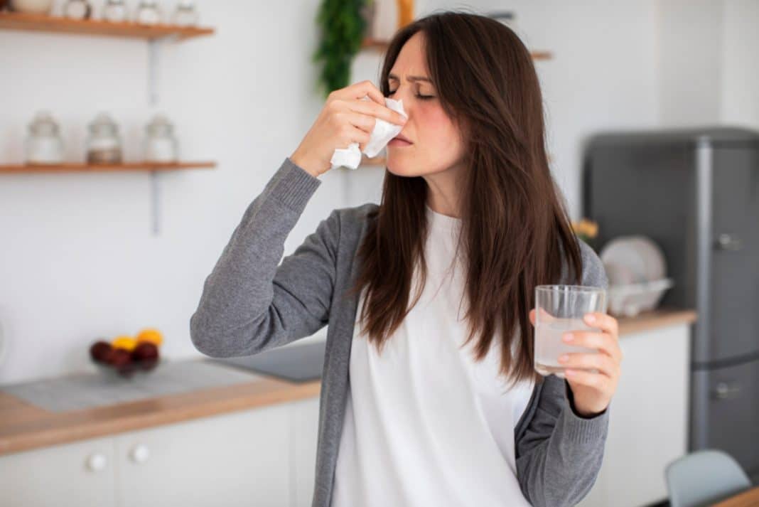 Kobieta trzyma chusteczkę przy nosie, wygląda na zatkaną i zacinającą się podczas kichania.