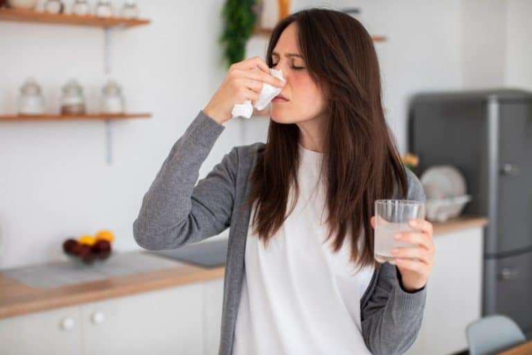 Kobieta trzyma chusteczkę przy nosie, wygląda na zatkaną i zacinającą się podczas kichania.