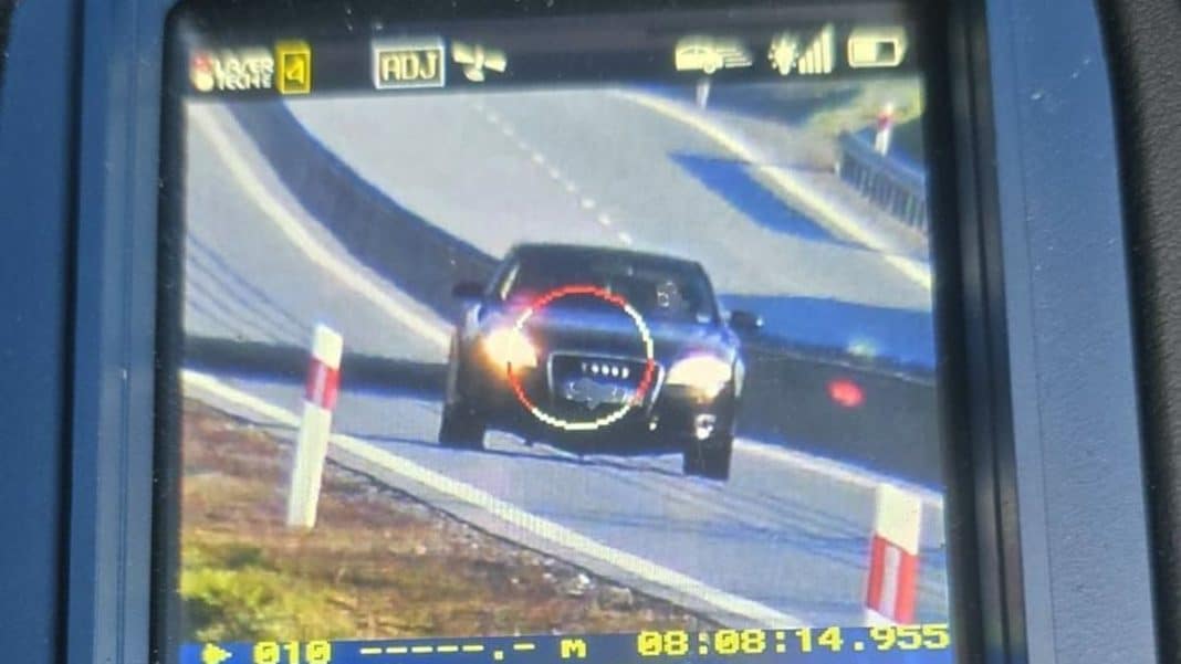 Zdjęcie z pomiaru prędkości na obwodnicy, pokazujące samoch&oacute;d z włączonymi światłami.