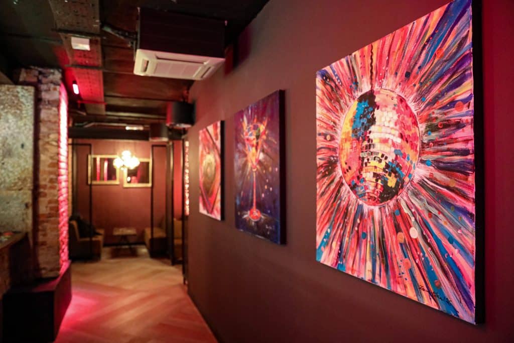 Wnętrze nowego klubu Dyskoteka Music Bar w Olsztynie, z kolorowymi obrazami na ścianach i ciepłym oświetleniem.