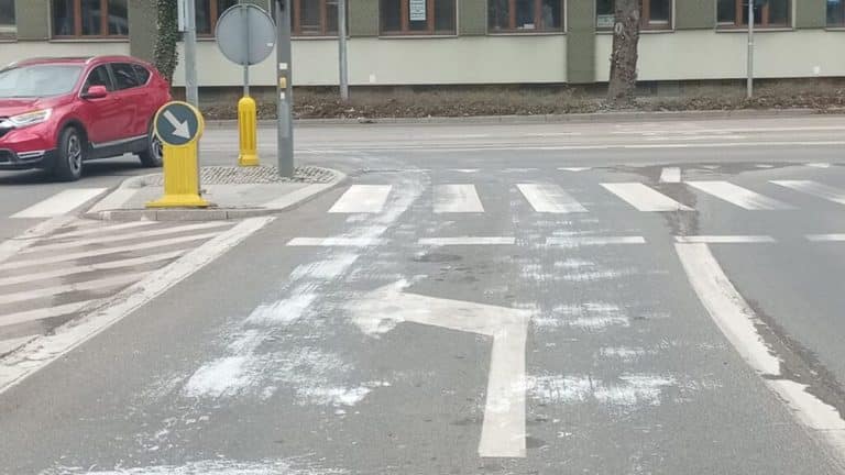 Ulica w Olsztynie z białą farbą rozlaną na jezdni i pasach dla pieszych.