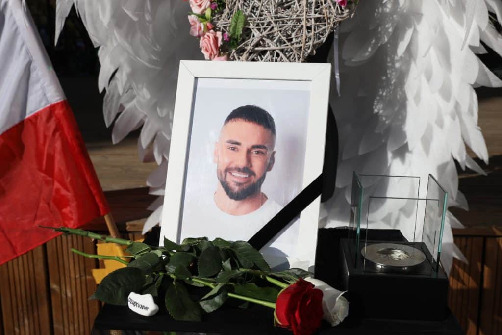 Zdjęcie na cmentarzu z portretem mężczyzny, kwiatami i zniczami, upamiętniające Łukasza Litewkę.