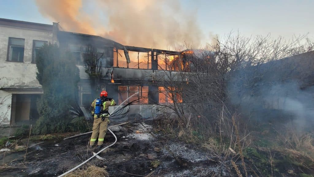 Strażak gasi pożar pustostanu przy ul. Junak&oacute;w w Elblągu, ogień trawi budynek, unoszą się kłęby dymu.