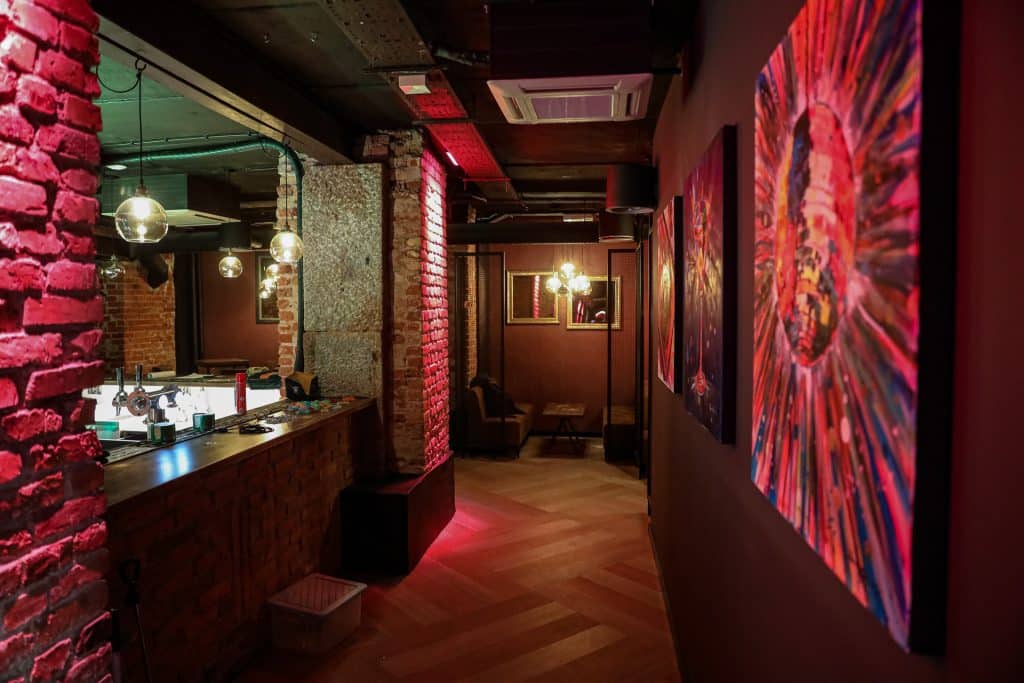 Wnętrze nowego klubu Dyskoteka Music Bar w Olsztynie, z czerwonymi ścianami, obrazami i oświetleniem.