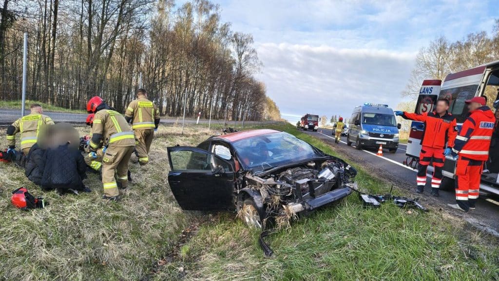 Wypadek samochodowy na drodze S22, ratownicy udzielają pomocy poszkodowanym przy uszkodzonym pojeździe.
