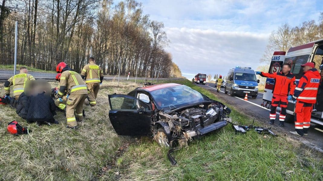 Wypadek samochodowy na drodze S22, ratownicy udzielają pomocy poszkodowanym przy uszkodzonym pojeździe.