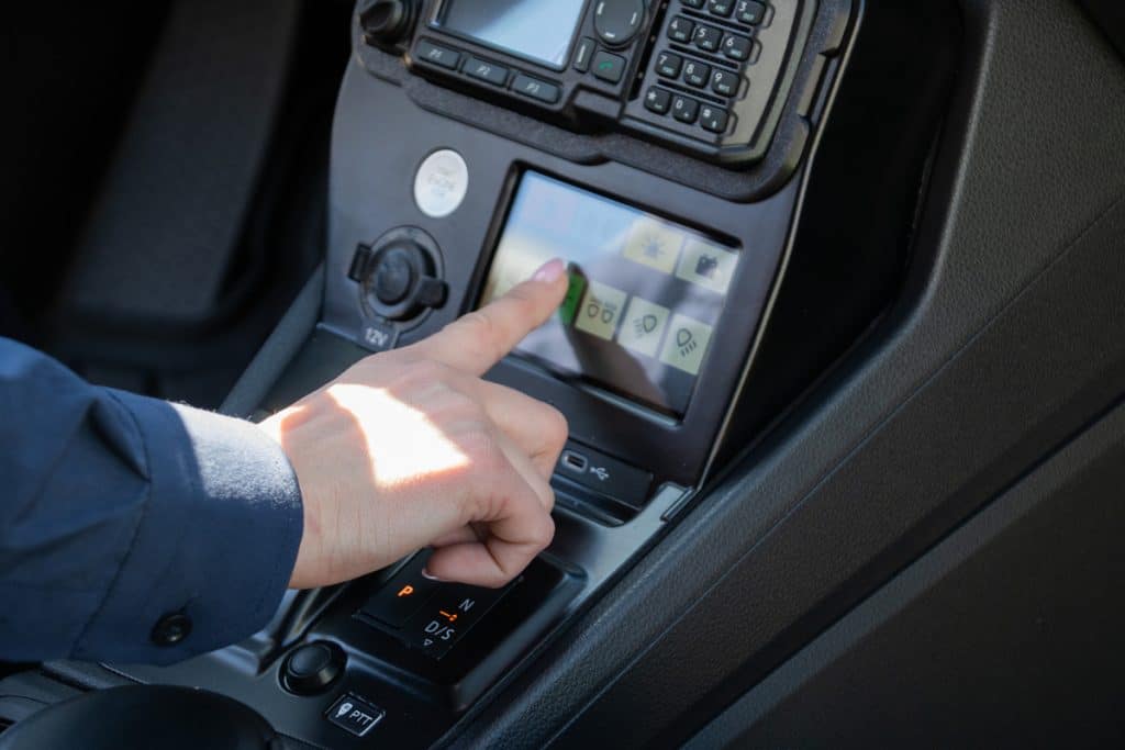 Wnętrze policyjnego samochodu z widocznym panelem sterowania i urządzeniami elektronicznymi.