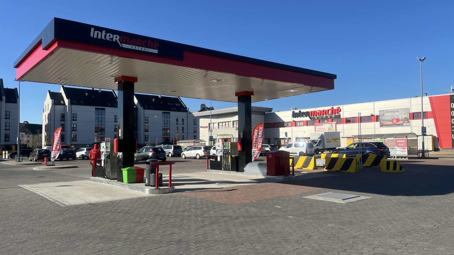 Stacja paliw Intermarch&eacute; Olsztyn z nowoczesną myjnią i dystrybutorami paliwa na tle sklep&oacute;w i parkingu.