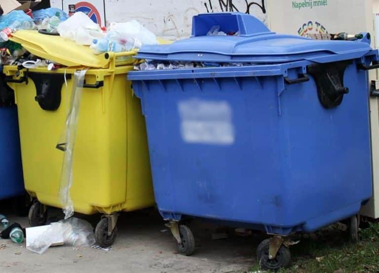 Na zdjęciu dwa pojemniki na odpady, żółty i niebieski, z odpadami i śmieciami wokół nich.