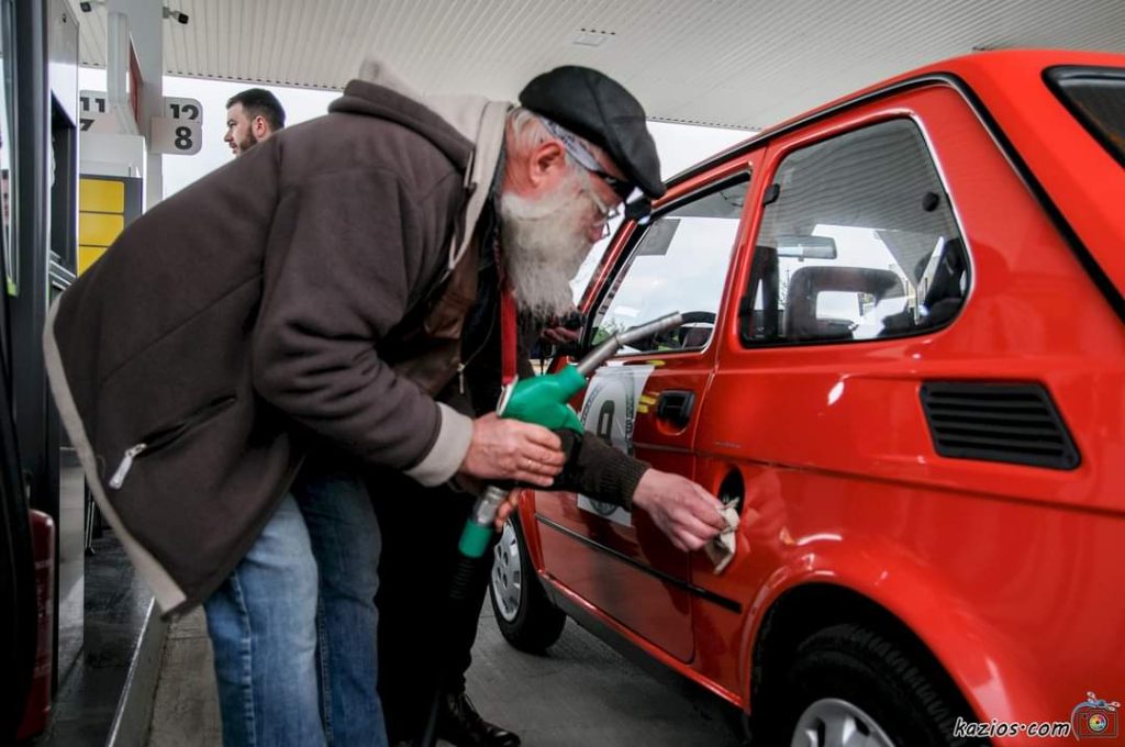 Mężczyzna myje samoch&oacute;d na stacji benzynowej, obok inny kierowca.
