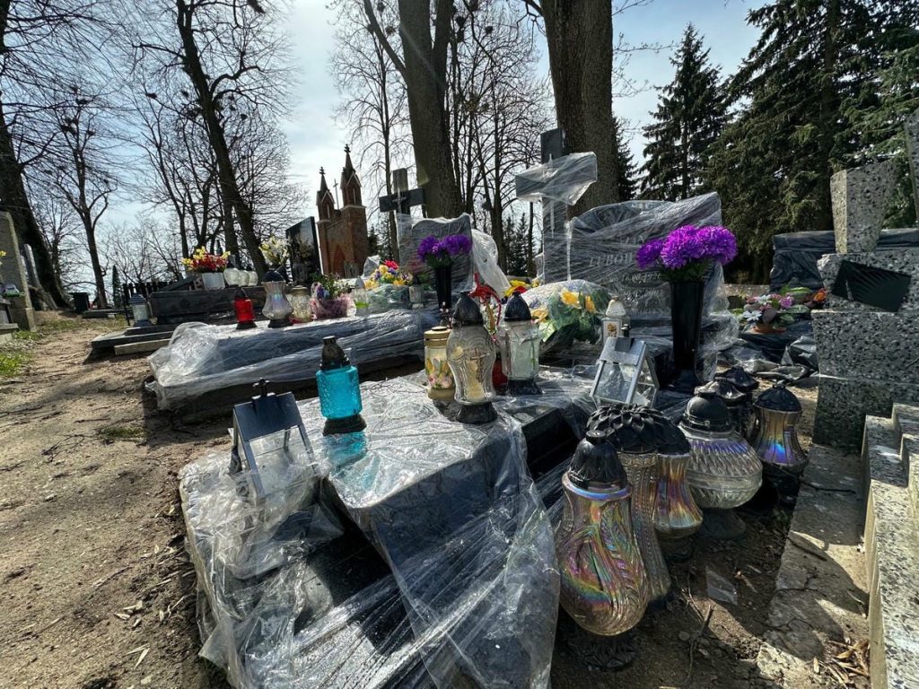 Nagrobki na cmentarzu w Jezioranach przykryte folią, wok&oacute;ł porozrzucane kwiaty i znicze.