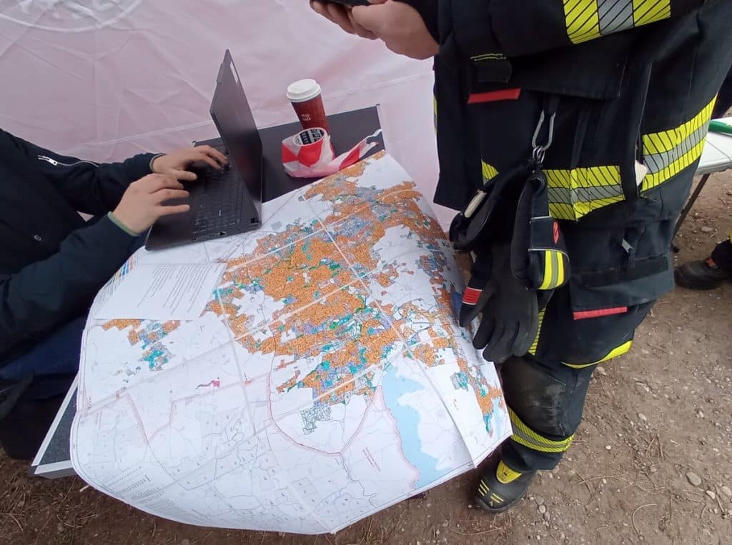 Strażak i urzędnik analizują mapę podczas akcji poszukiwawczej w terenie.