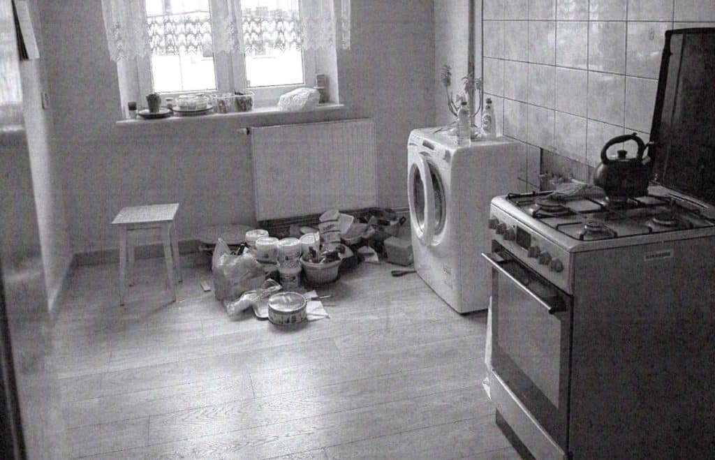 Puste mieszkanie z kuchnią, na podłodze porozrzucane przedmioty i sprzęty, w tym pralka i kuchenka.