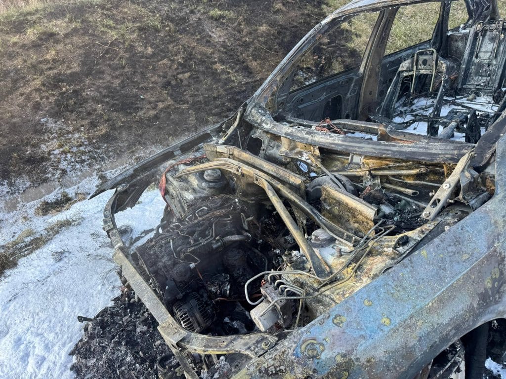 Spalony samoch&oacute;d marki Audi na drodze ekspresowej, widoczny zniszczony i wypalony po pożarze.