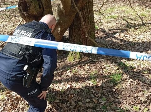 Policjant bada teren w lesie, zabezpieczając miejsce znaleziska podczas interwencji.