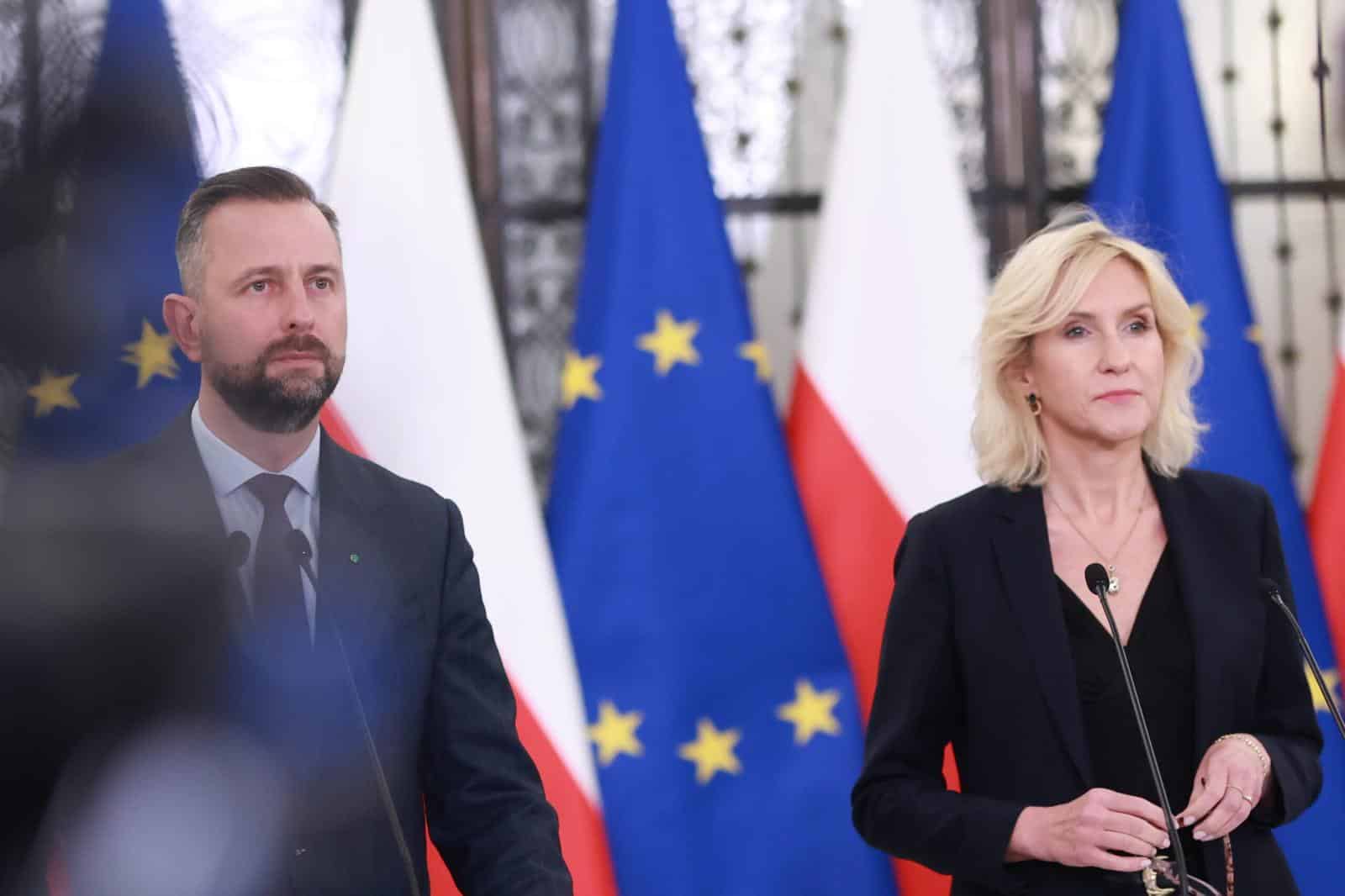 Dwoje polityków stoi przy mikrofonach, za nimi flagi Polski i Unii Europejskiej.