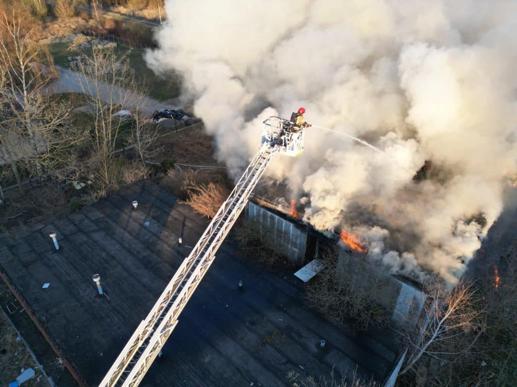 Strażak na dźwigu gaśniczym walczy z pożarem pustostanu w Elblągu, unosząc się nad płonącym budynkiem.