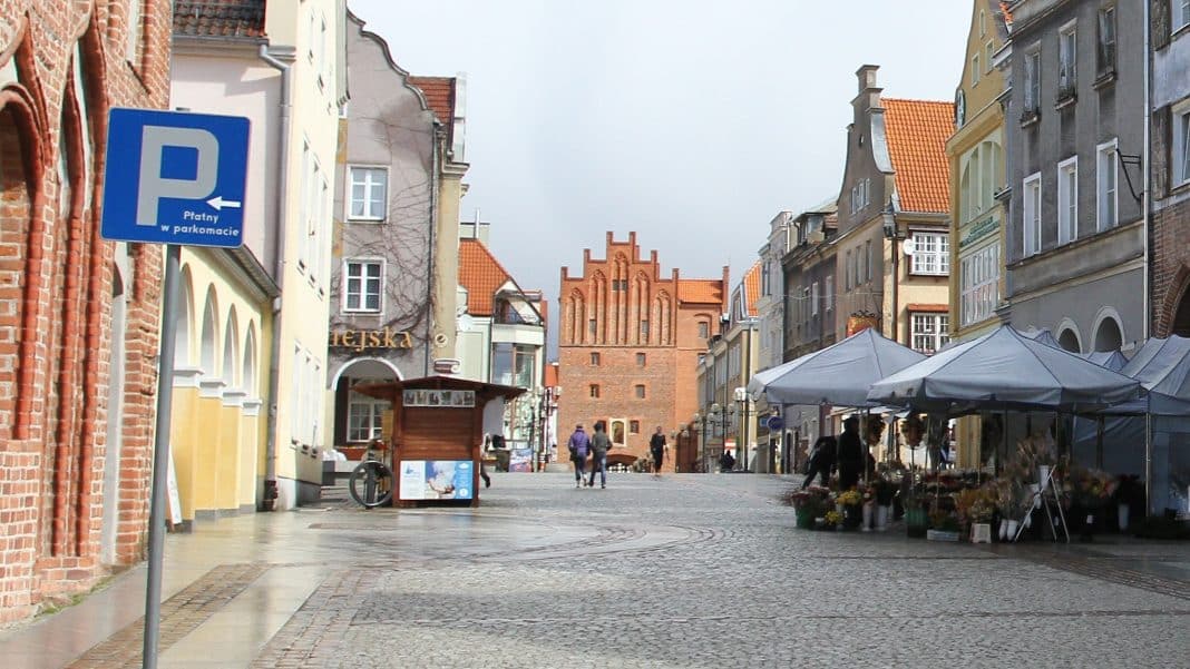 Widok na star&oacute;wkę w Olsztynie z placem i budynkami, w tle widoczna ceglana wieża.