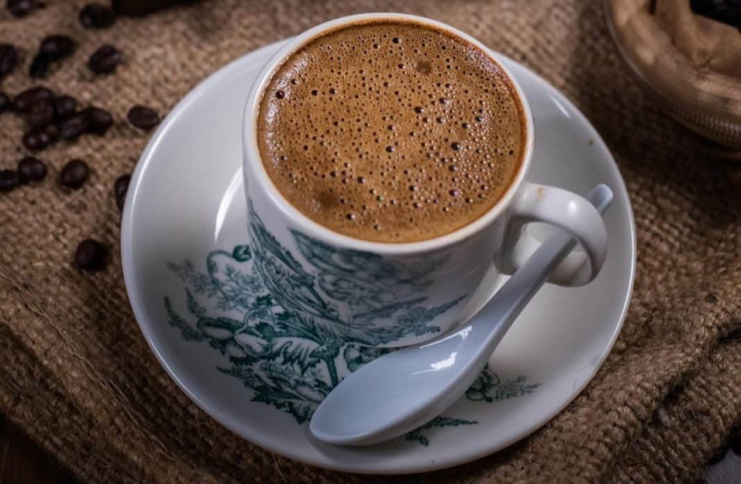 Filiżanka kawy na talerzyku z łyżeczką, na tle tekstury materiału i ziaren kawy.