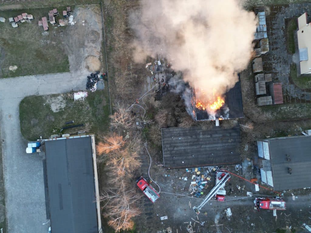 Zdjęcie z powietrza pokazujące pożar pustostanu w Elblągu, z widocznymi strażakami i sprzętem gaśniczym.
