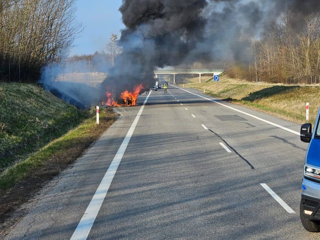 Samoch&oacute;d marki Audi płonie na drodze ekspresowej, z widocznym czarnym dymem unoszącym się w powietrze.