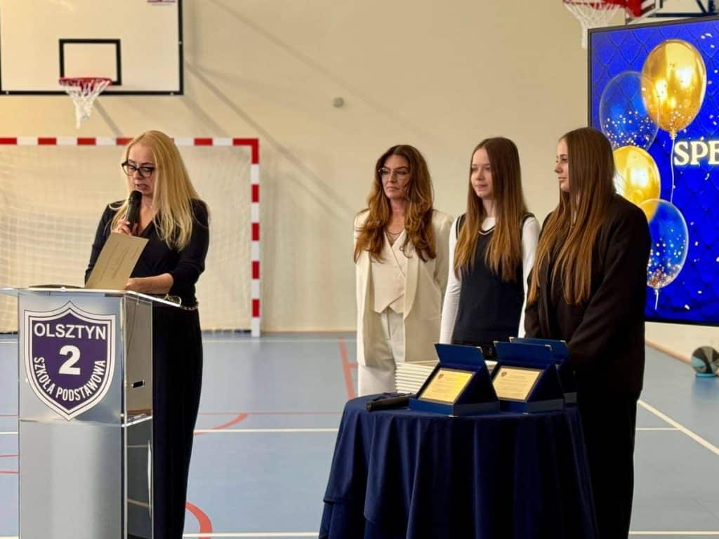 Uczniowie i nauczycielka podczas uroczystości otwarcia nowej hali sportowej w szkole podstawowej w Olsztynie.