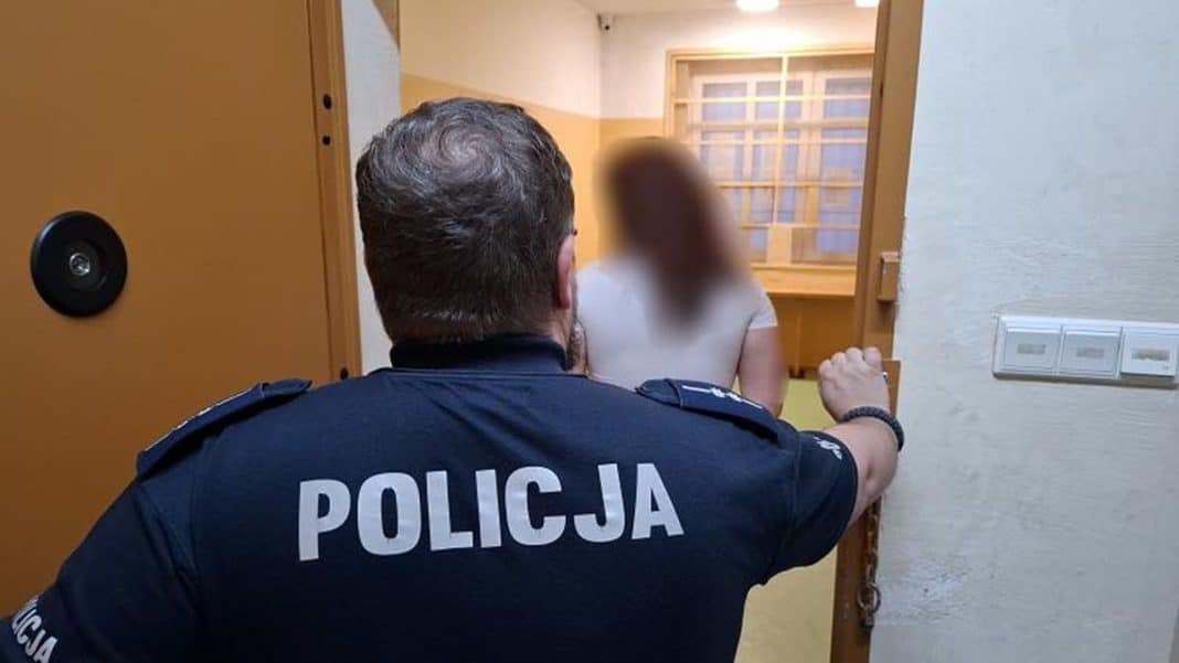 Policjant zatrzymuje kobietę w drzwiach, jej twarz jest zamazana.