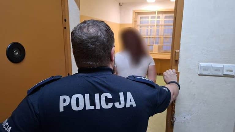 Policjant zatrzymuje kobietę w drzwiach, jej twarz jest zamazana.