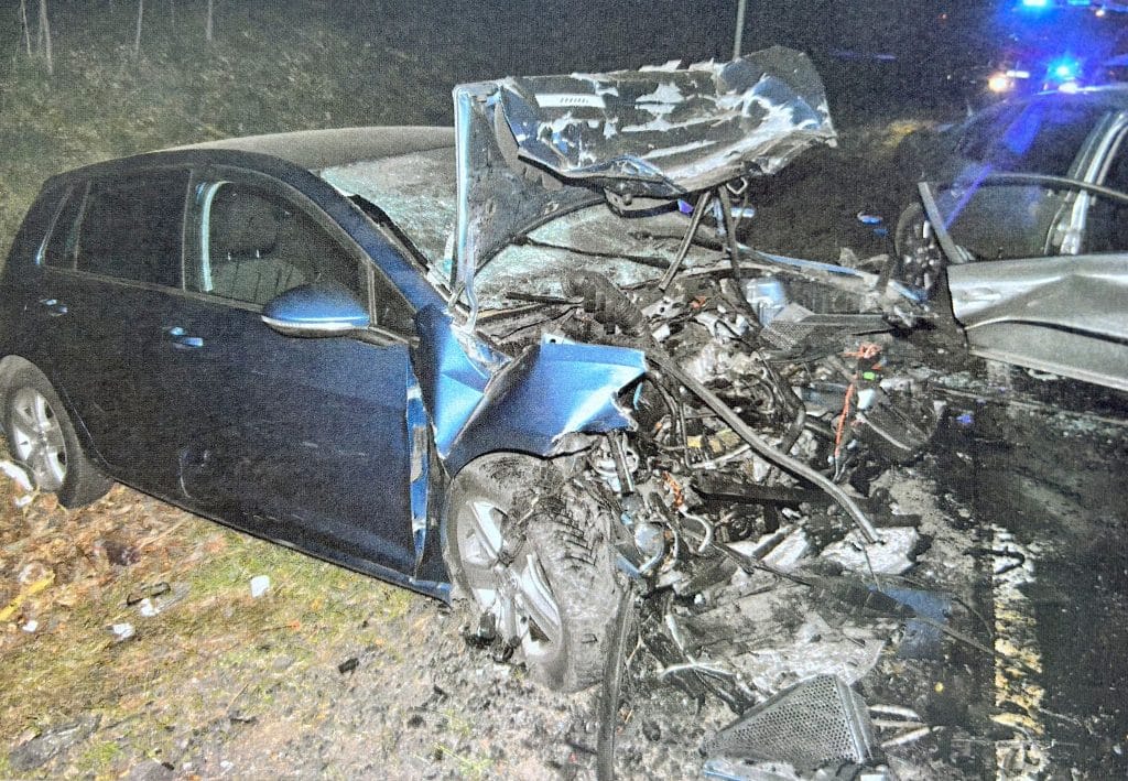 Rozbity samoch&oacute;d po czołowym zderzeniu na drodze krajowej, widoczne zniszczenia karoserii i silnika.