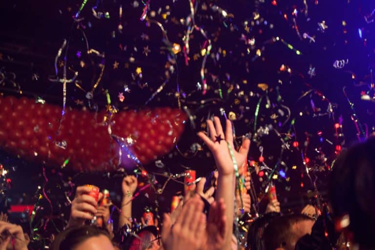 Tłum ludzi na scenie podczas pokazu confetti i efekt&oacute;w specjalnych, z kolorowymi serpentynami i konfetti w powietrzu.