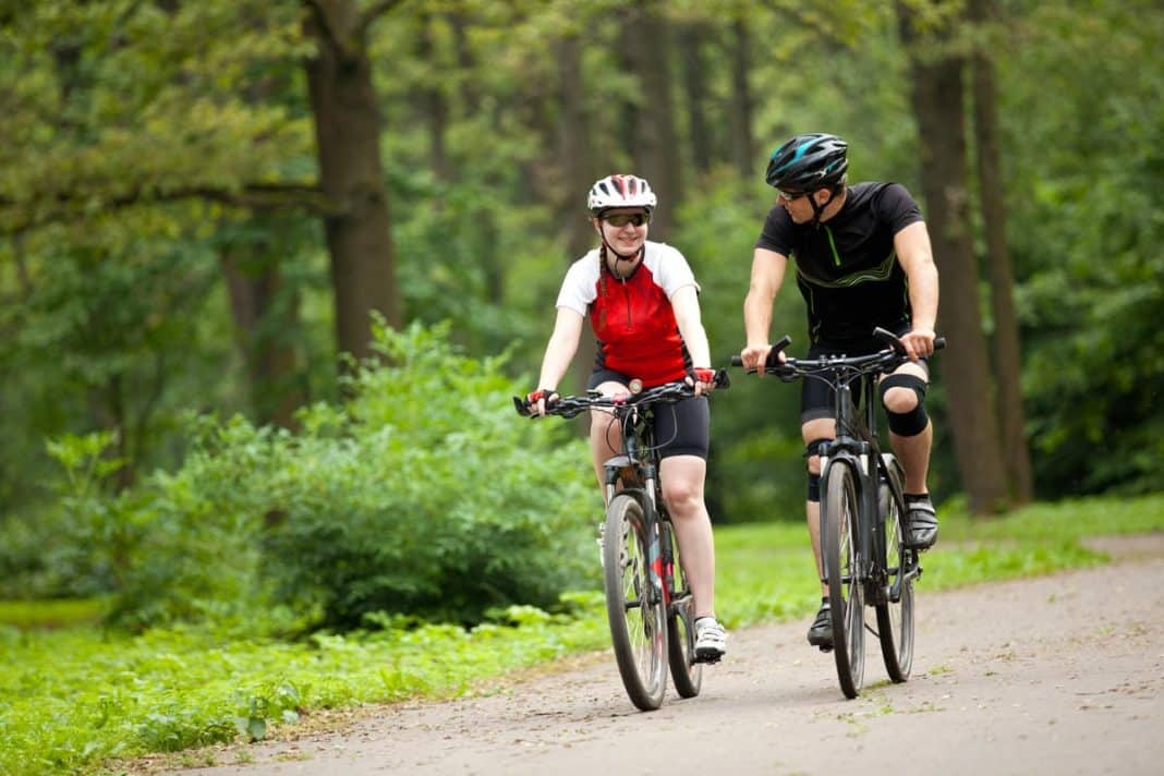 Dwoje rowerzyst&oacute;w na ścieżce w lesie, uśmiechają się i rozmawiają podczas jazdy.