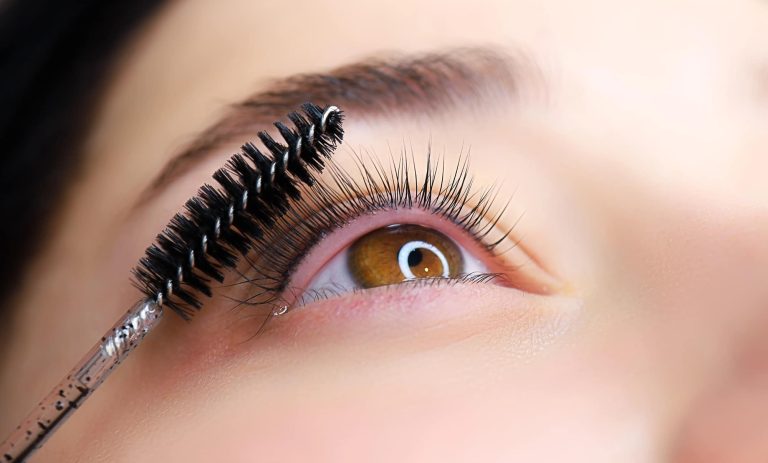 Zdjęcie pokazuje osobę czyszczącą rzęsy szczoteczką z tuszem, skupiając się na oku.